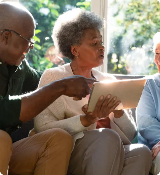 A group of three older individuals looking at a digital tablet together.